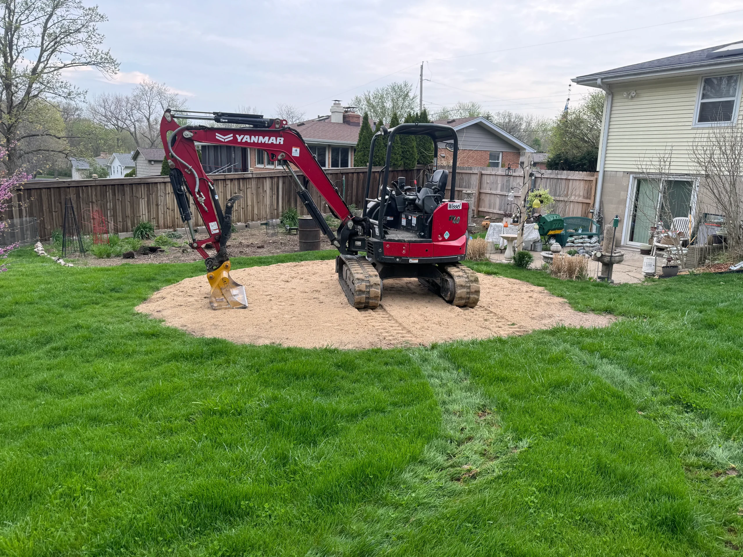 Yanmar Excavator on a Sand Base in a Backyard Red Yanmar excavator positioned on a sand base in a residential backyard.
